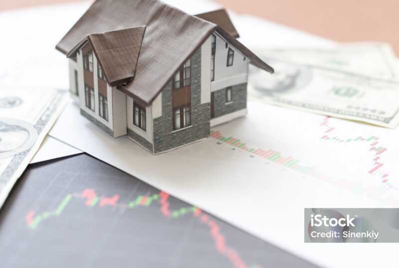 uma casa em miniatura em cima de papéis que ilustam as ocilações do mercado