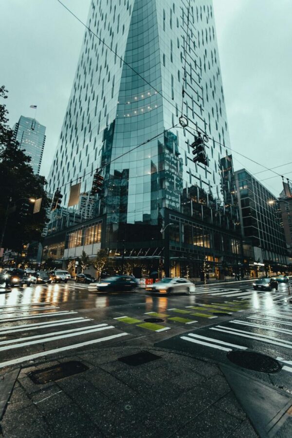 uma rua com akguns carros, um céu nublado e um prédio alto