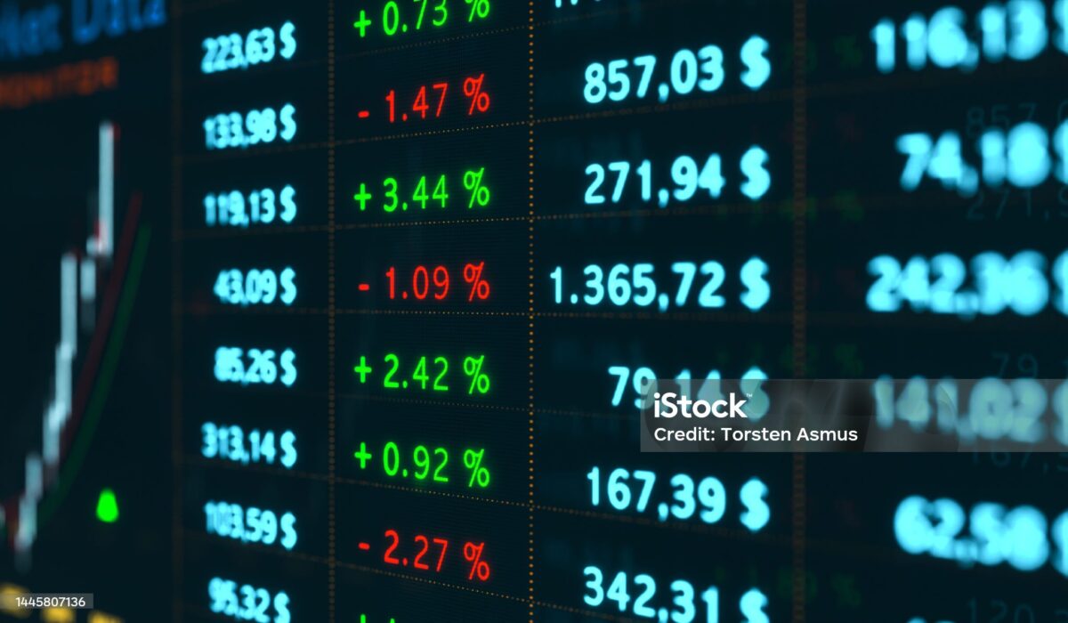 A imagem mostra um painel digital do mercado financeiro, exibindo cotações, preços e variações percentuais de ativos. Na tela, é possível ver: Valores em dólares ($) destacados em azul-claro, representando preços ou cotações de diferentes ativos. Percentuais em verde com sinal de “+”, indicando valorização (ex.: +0,73%, +3,44%, +2,42%). Percentuais em vermelho com sinal de “-”, indicando desvalorização (ex.: -1,47%, -1,09%, -2,27%). Do lado esquerdo, há um gráfico de velas (candlestick) parcialmente visível, que reforça a ideia de análise técnica do mercado. O ambiente sugere um painel de bolsa de valores ou mercado de câmbio, típico de sistemas de negociação usados para acompanhar oscilações em tempo real. A estética é tecnológica, dinâmica e voltada para investimentos, transmitindo o movimento constante do mercado financeiro.