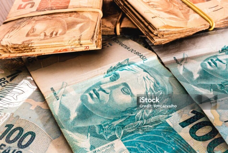 Essa imagem mostra diversas cédulas de reais (R$), a moeda oficial do Brasil. Ela retrata um conjunto de notas de dinheiro, com destaque para as cédulas de R$ 100 (azul esverdeado, com a efígie da República) e R$ 50 (marrom alaranjado, com a imagem da onça-pintada no verso, não visível na foto).