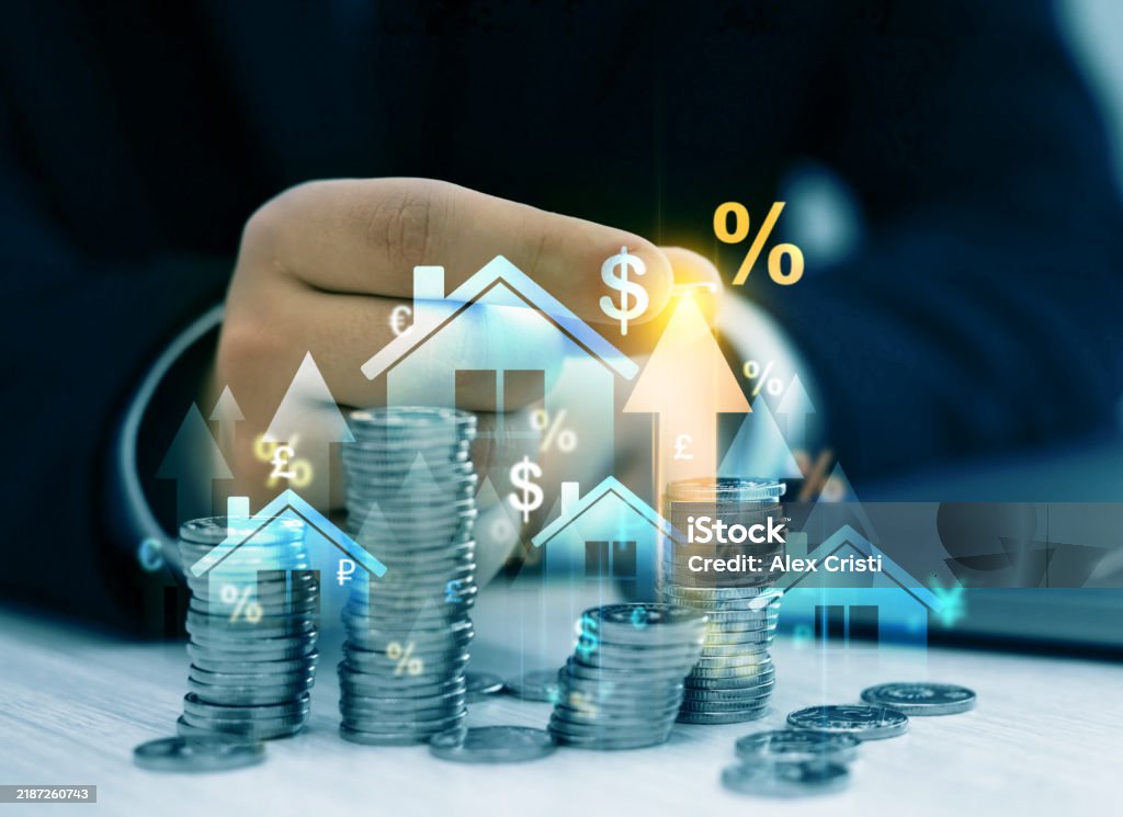 A imagem mostra uma mão em destaque, parcialmente fechada, atrás de várias pilhas de moedas empilhadas em diferentes alturas, sugerindo crescimento financeiro ou investimento. Sobre a foto há ícones gráficos transparentes, como casas, setas apontando para cima, cifrões, símbolos de moedas estrangeiras (€, £, $) e porcentagens (%). A composição transmite ideias relacionadas a finanças, investimentos, mercado imobiliário, crescimento de patrimônio e taxas de juros. A presença das casas sugere uma ligação com financiamento ou investimento imobiliário, enquanto as setas e símbolos percentuais remetem a valorização e rentabilidade.