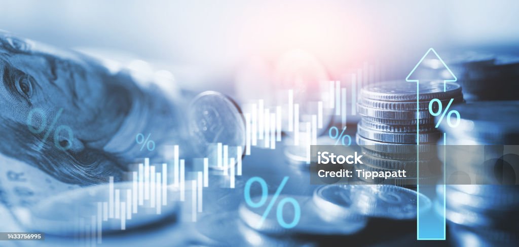 A imagem mostra uma composição visual relacionada ao dinheiro e economia. À esquerda, aparece parte de uma cédula de real (com o rosto característico das notas brasileiras), e à direita há várias pilhas de moedas empilhadas em diferentes alturas, representando crescimento financeiro. Sobre a cena, estão sobrepostos elementos gráficos digitais: Símbolos de porcentagem (%), sugerindo juros, inflação ou taxas econômicas. Um gráfico de barras/linhas ascendentes, indicando alta nos indicadores financeiros. Uma seta azul apontando para cima, reforçando a ideia de crescimento, aumento de juros ou valorização monetária. O tom da imagem é azulado, transmitindo uma estética moderna e tecnológica, muito usada em ilustrações de economia, investimentos e finanças.